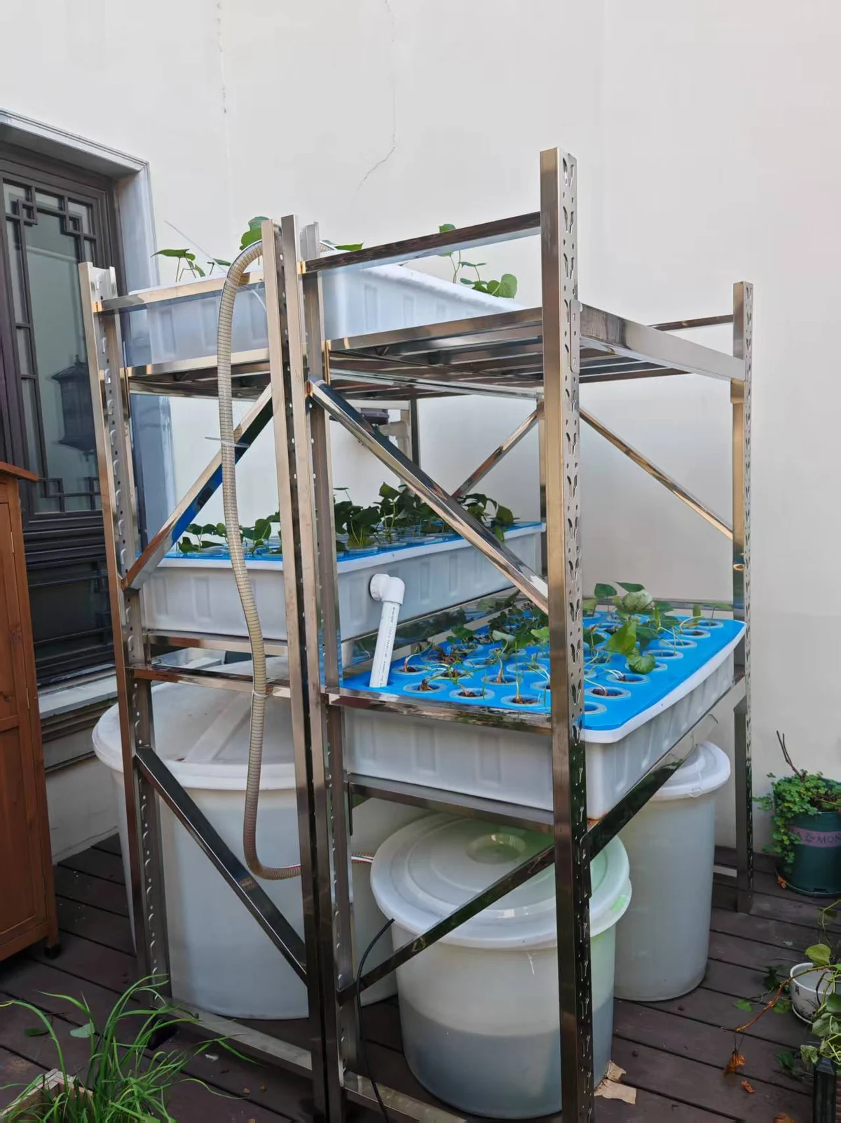 Vertical modular aquaponics tower with stacked grow beds, grey fish tanks and stainless steel support frame